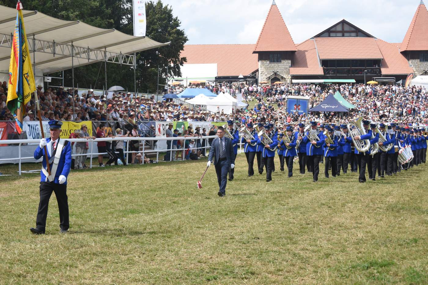 La fanfare la Collongienne, de Collonges en Valais, défile en uniforme bleu devant des tribunes pleines