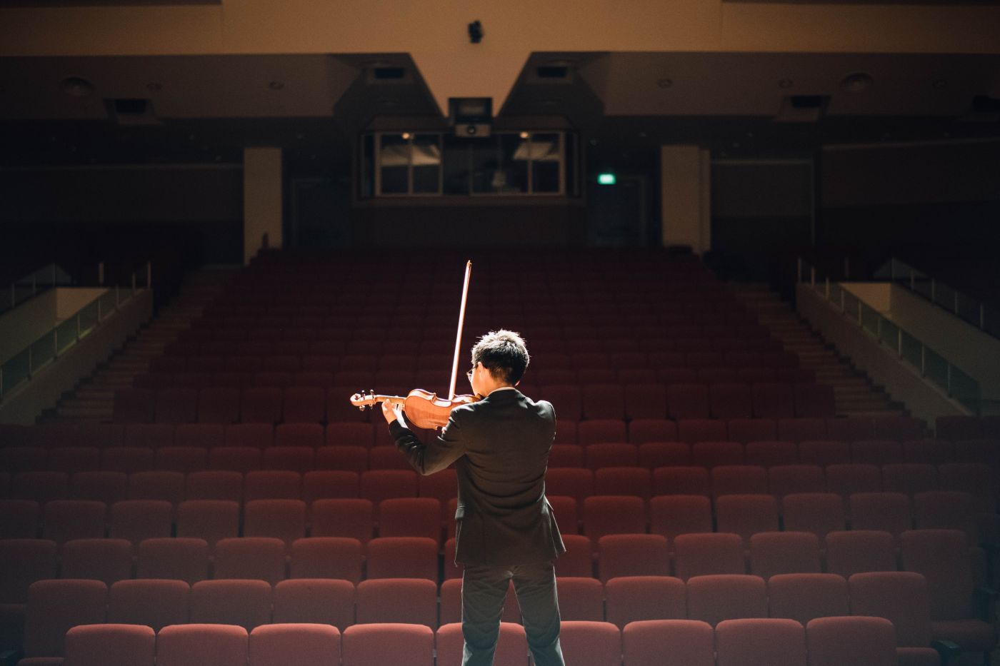 Un violoniste répète seul sur scène, face à une salle vide aux fauteuils rouges
